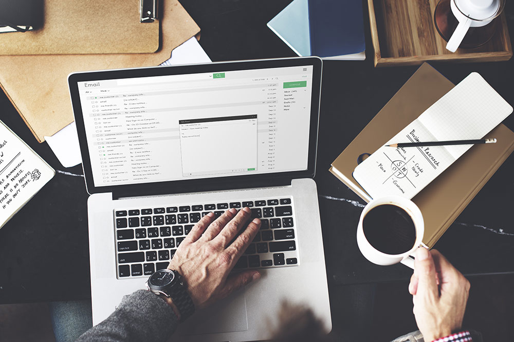 Man on laptop with coffee in hand looking at email