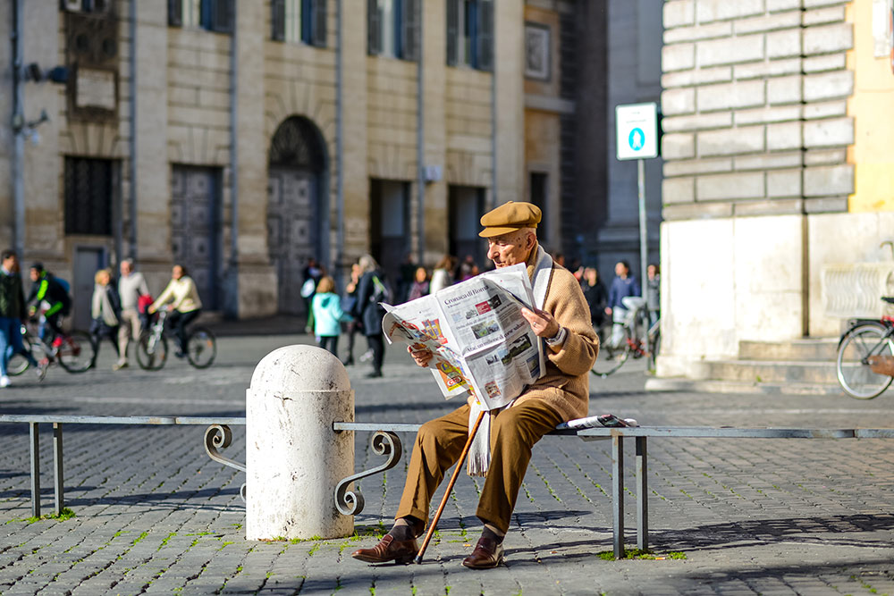 Senior man sitting on bench outside reading the newspaper