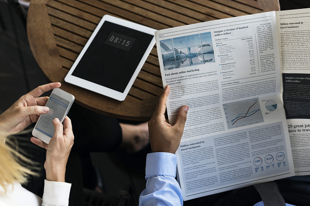 Man reading newspaper and woman reading news on smartphone at table