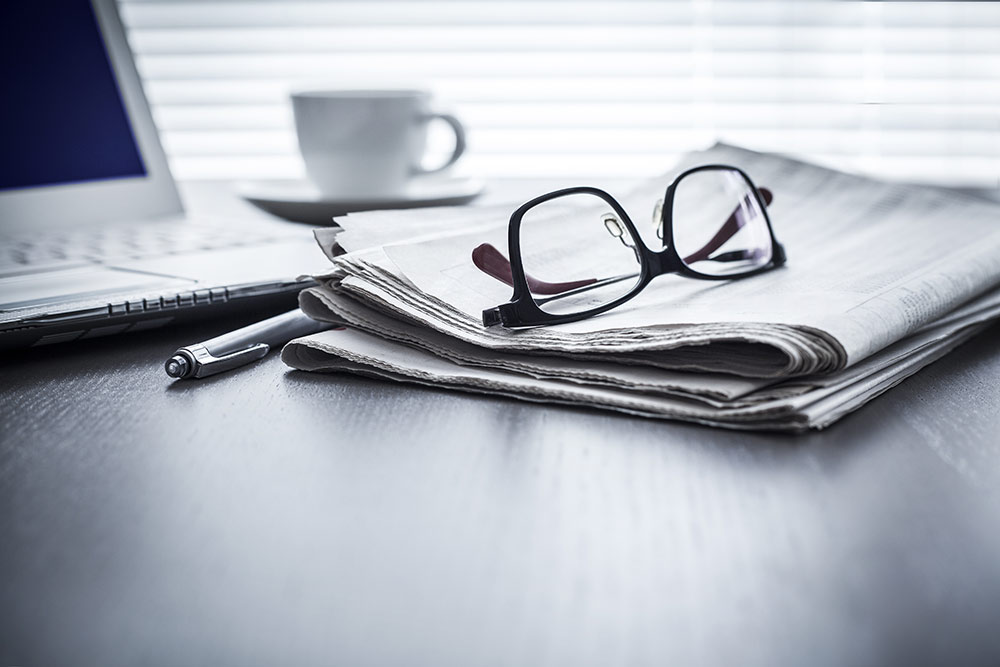 Newspaper sitting on desk with glasses sitting on top of newspaper