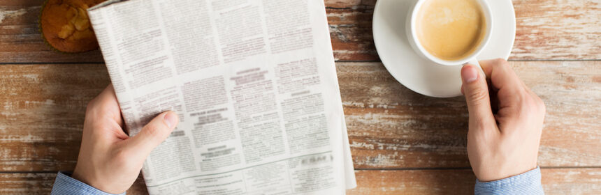 A woman drinking coffee while reading the newspaper