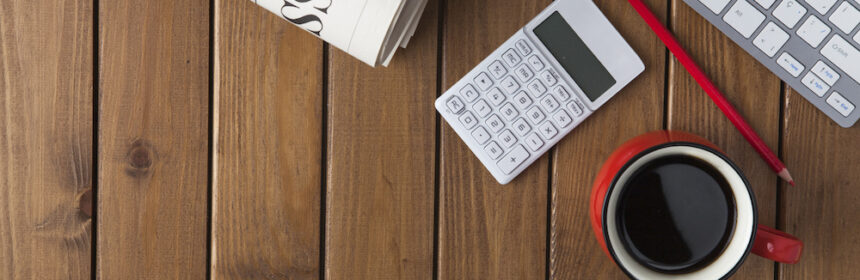 A newspaper, coffee cup, and calculator sit on a computer desk