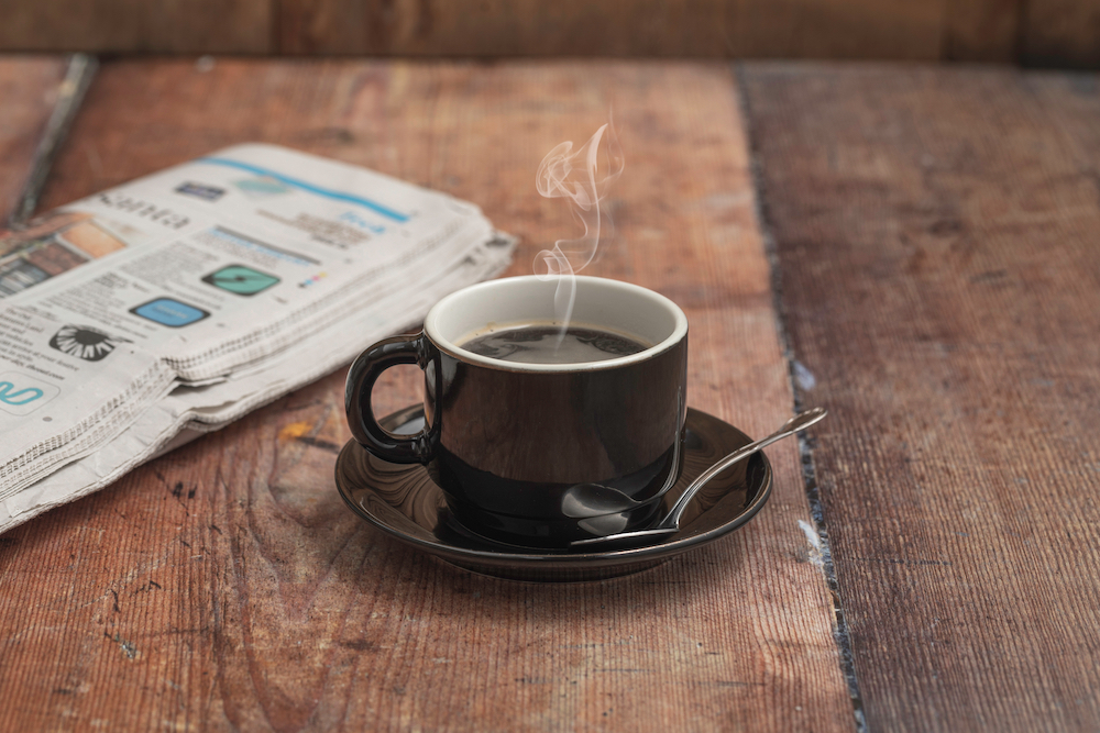 A steaming cup of coffee with a newspaper