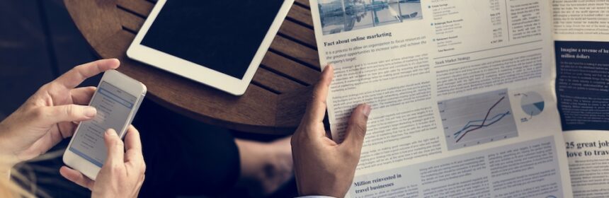 A man reading print advertising in a newspaper while a woman uses social media on her phone