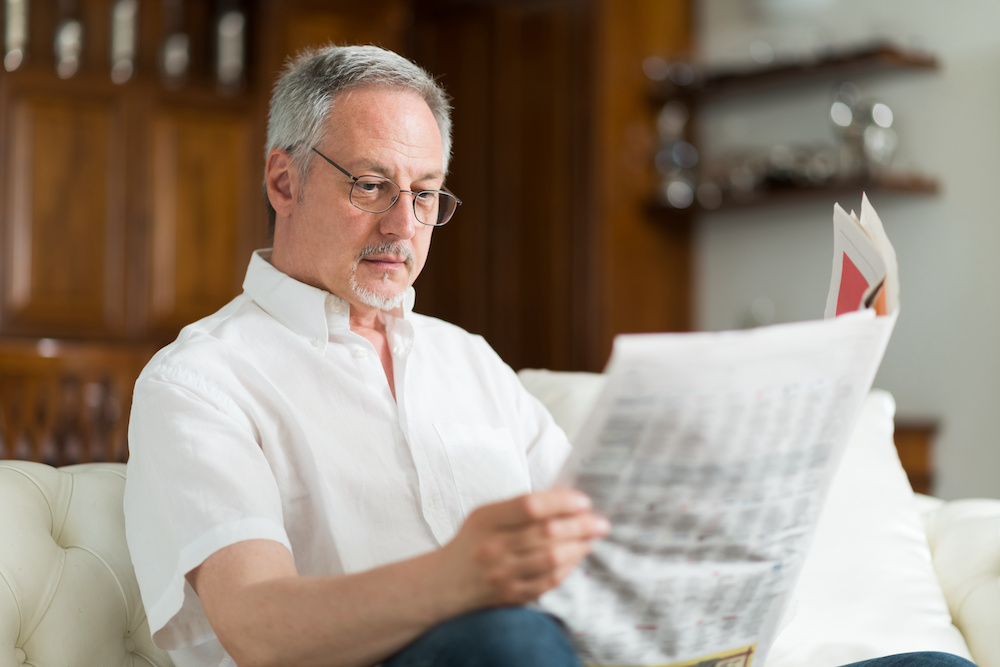 An older man reading through the local business advertising in his newspaper