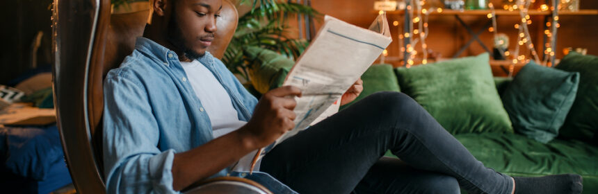 A young man reading a newspaper in a cozy apartment