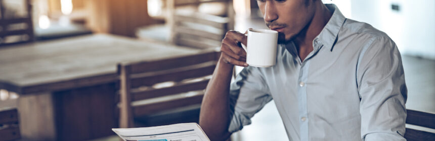 A hip young man drinking coffee while reading a newspaper